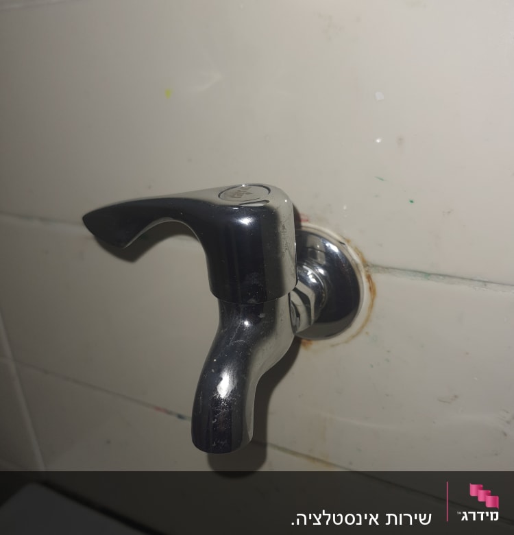 ברז מתכת מותקן על קיר אריחים לבנים